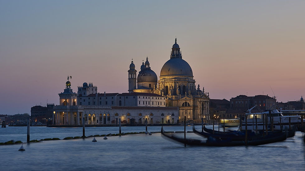 Venice's Santa Maria della Salute at sunset. Calm water with moored gondolas in foreground. Warm glow, serene evening mood.