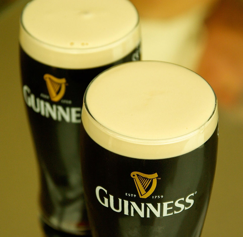 Two pint glasses of Guinness with creamy foam on top. Black logo with harp symbol visible. Bright, inviting atmosphere.