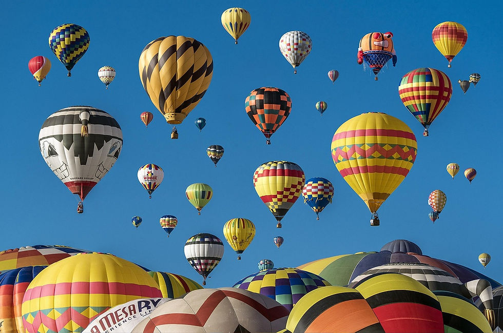 Colorful hot air balloons of various patterns float against a clear blue sky, creating a vibrant and joyful scene.