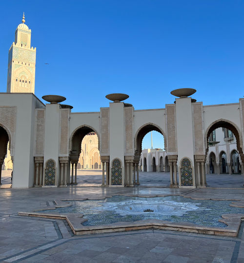 Early morning photo of the empty courtyard with Moroccan tiles in the foreground. The marble arched entrances to the Mosque are in the background