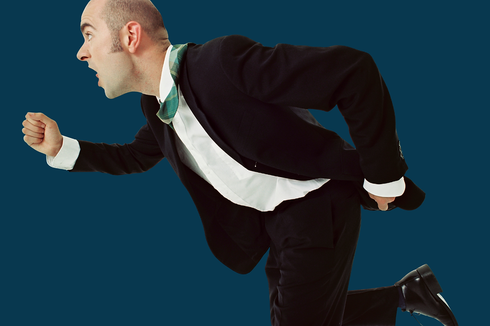 Bald man in a black suit sprints forward against a plain blue background, looking surprised.