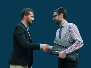 Two young businessmen shake hands in front of a dark blue background.