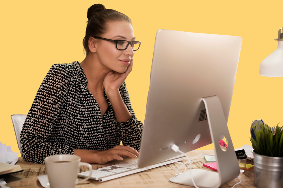 Woman with glasses rests her chin while working at a desktop computer, with a mug and plant on a wooden desk against a yellow background.