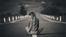 Femme assise seule sur une route, vue de dos, en noir et blanc, symbolisant la confusion et la quête de soi à 40 ans