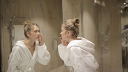 Une femme d'une quarantaine d'années, en peignoir blanc, se regarde longuement dans le miroir de sa salle de bain. Son regard est introspectif, comme si elle cherchait à se reconnaître.