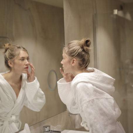 Une femme d'une quarantaine d'années, en peignoir blanc, se regarde longuement dans le miroir de sa salle de bain. Son regard est introspectif, comme si elle cherchait à se reconnaître.