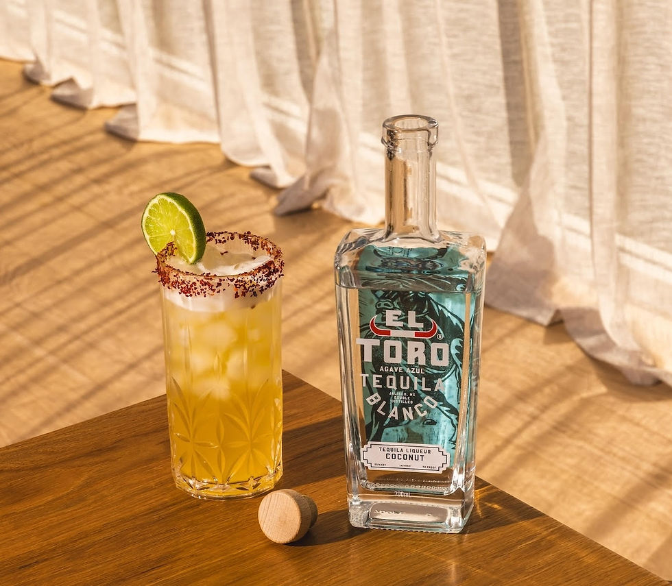 Tequila bottle and margarita glass with lime on a wooden table. Sunlit room with sheer curtains. Vibrant summer vibe.