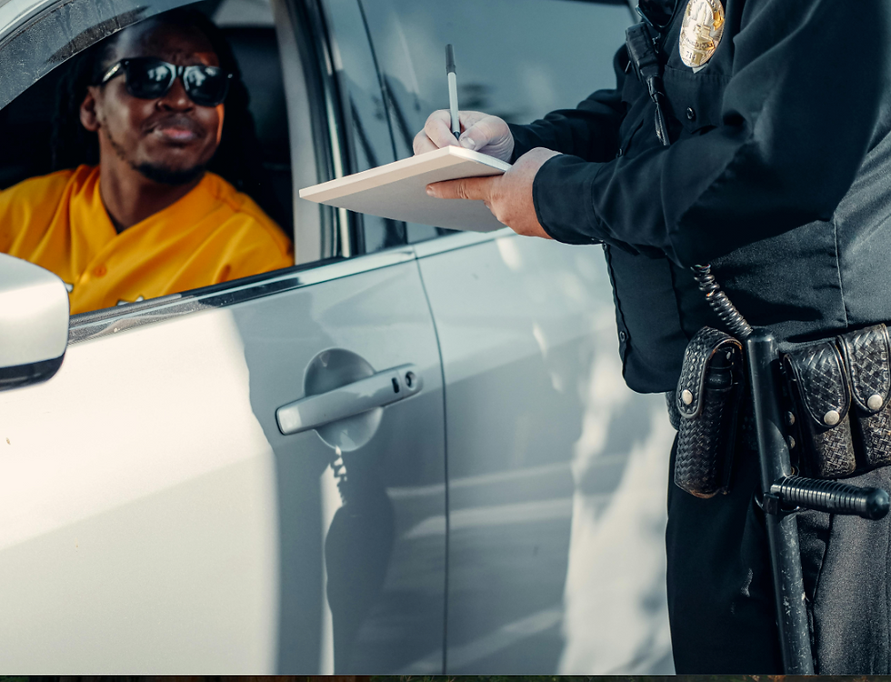 A person in a yellow shirt and sunglasses sits in a car, while a police officer writes a note. The mood appears calm.