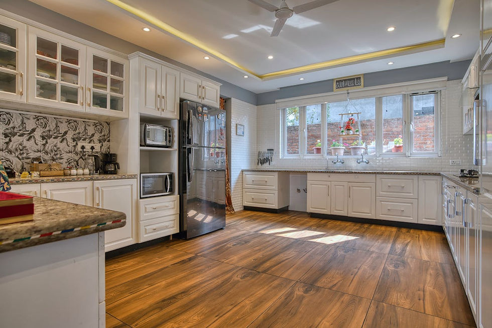 Modern kitchen with white cabinets, wooden floor, and large windows. Black fridge, microwave, and a floral backsplash enhance the space.
