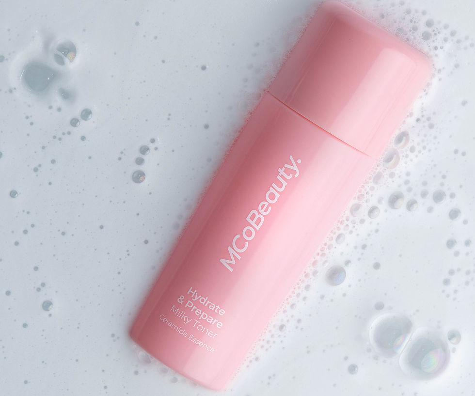 Pink MCoBeauty toner bottle on a foamy white background with bubbles. Text reads "Hydrate & Prepare Milky Toner Ceramide Essence".