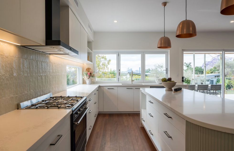 Bright modern kitchen with white island, copper pendant lights, and large windows overlooking a garden.