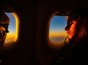 Woman gazing out of an aeroplane window at a golden sunset above the clouds