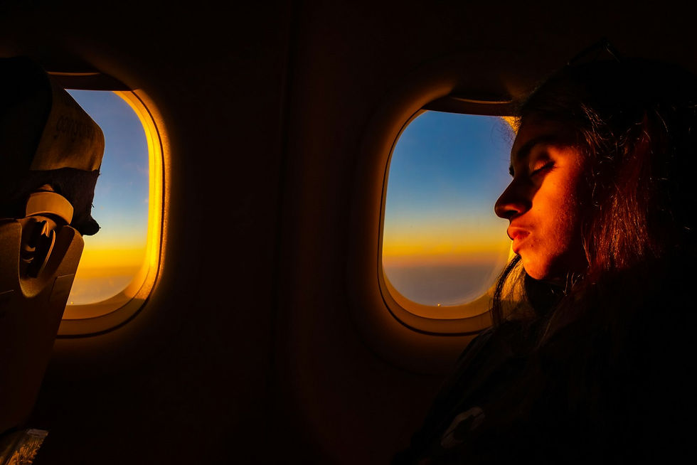 Woman gazing out of an aeroplane window at a golden sunset above the clouds