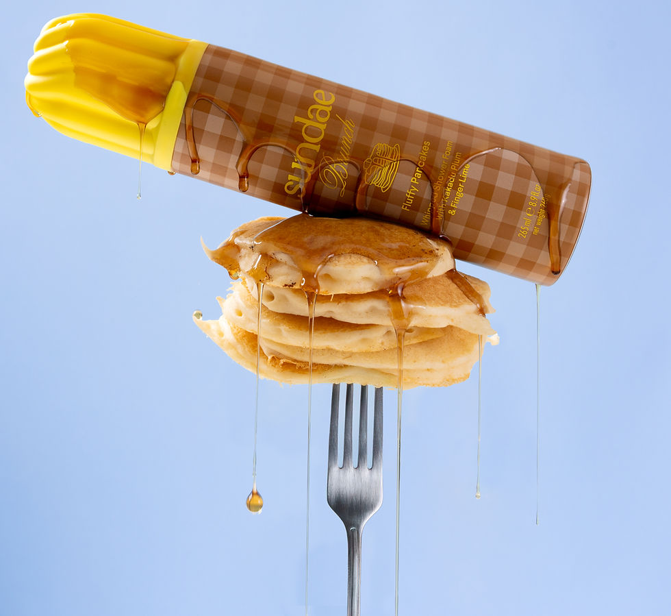 A stack of pancakes on a fork with syrup dripping from a tilted bottle above, set against a light blue background. The bottle is checkered.