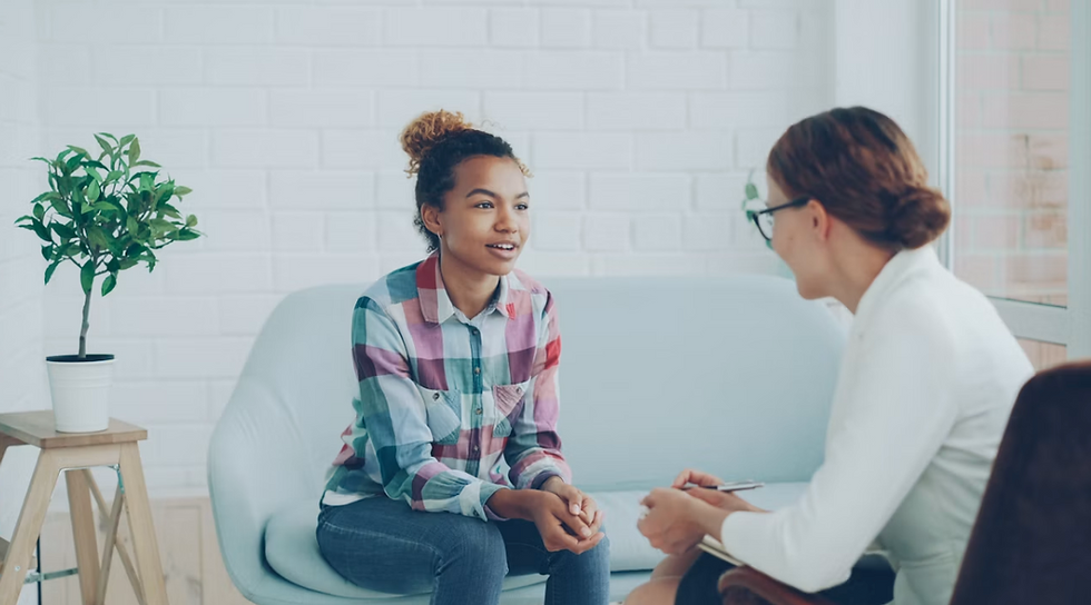 Young woman talks with a therapist on a light blue couch in a bright office with a potted plant, calm and supportive.