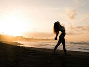 Silhouette of a woman stretching her arms wide on the seashore as the sun rises behind her