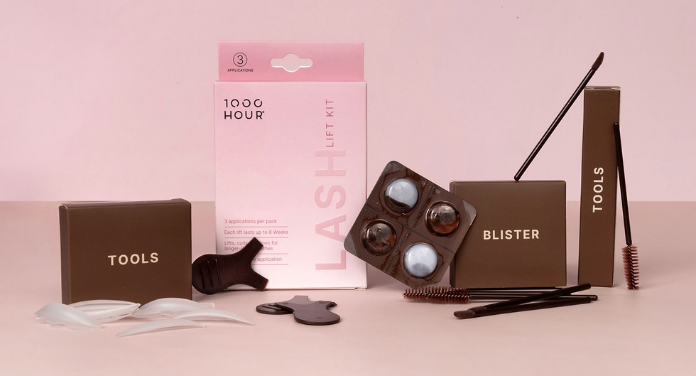 Eyelash lift kit on pink surface featuring pink and brown packaging labeled "LASH LIFT KIT," "TOOLS," and "BLISTER," with brushes and pads.