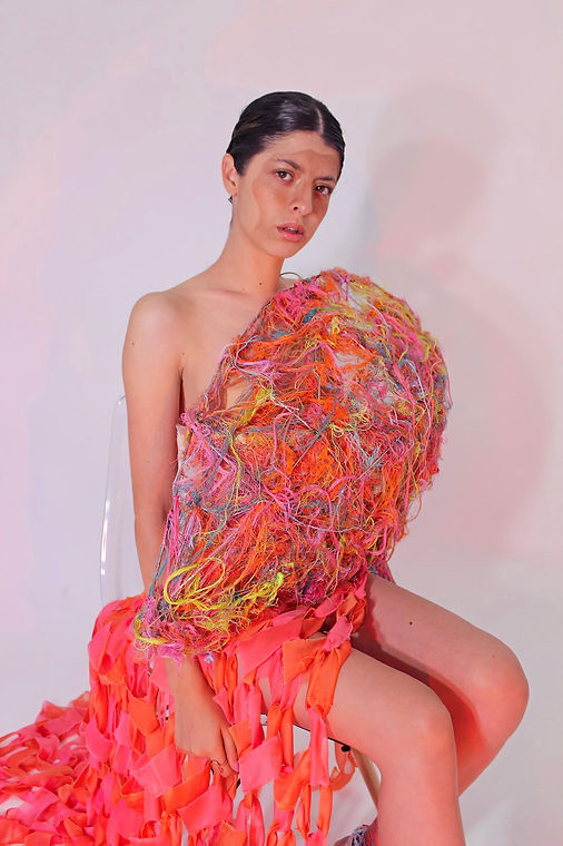 Una mujer sentada encima de una silla cubierta de hilos coloridos y falda de tela entrelazada.