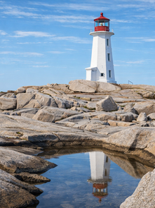 White lighthouse with red top on rocky coast, reflected in a tide pool under a clear blue sky