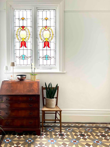 vintage bureau and antique chair stand proudly in front of an original stained glass window, all complimented by original Minton floor tiles