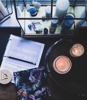 The Happy Story Bible worksheet binder on a desk, surrounded by candles and crystals, a free character and world-building planner for fantasy authors