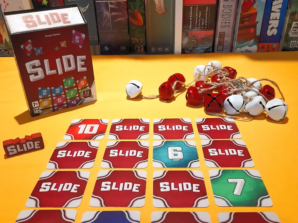 Game “SLIDE” on a yellow table with red and green cards, numbered dice, and red-white bells. Background shows various board games.