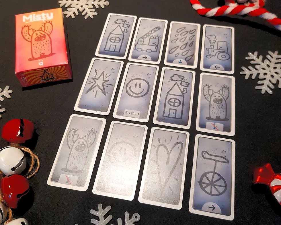 Cards with playful drawings arranged in rows on a black surface. A red box labeled "Misty" and festive decorations are nearby.