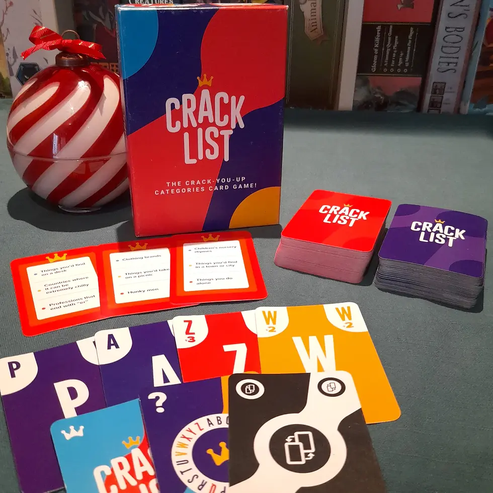 Crack List card game display with colorful decks and cards on a table. A red and white striped ornament sits beside the game box.