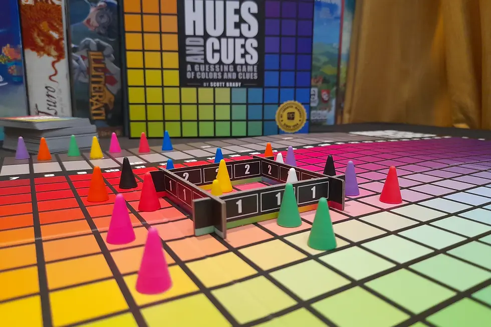 A colorful board game setup with cone markers on a color grid. The "Hues and Cues" box is in the background.