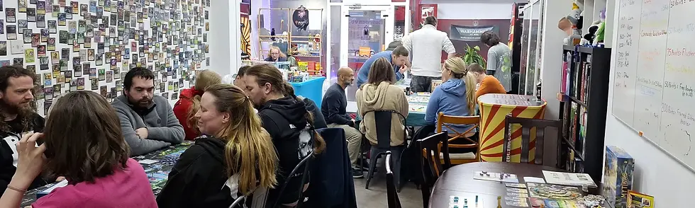 People are gathered in at a Big Top Board Game Mini Convention in Retrocave in Poole playing board games. The walls are covered with card displays.