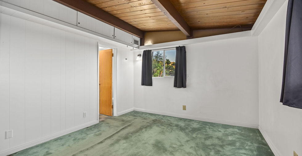 Bedroom with wood ceiling beams, laminate flooring, and natural light