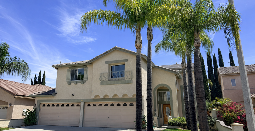 Front exterior of two-story home with three-car garage, arched entryway, stucco finish, and palm trees in landscaped yard.