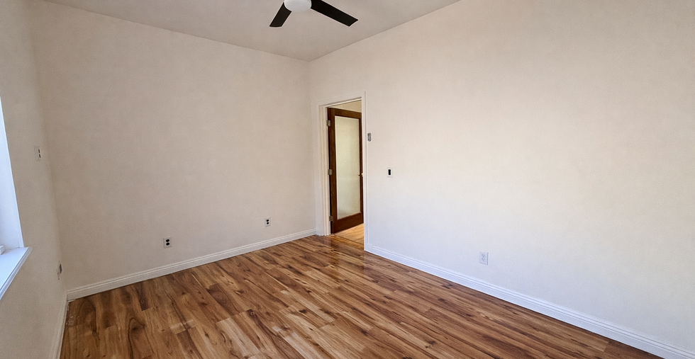 Downstairs bedroom with wood flooring, ceiling fan, neutral walls, and window for natural light.