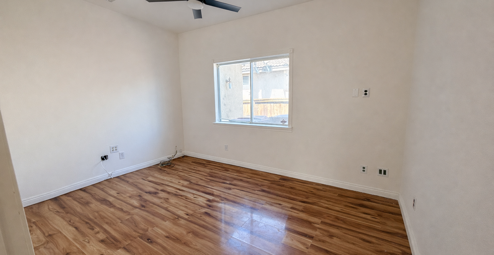 Downstairs bedroom with wood flooring, ceiling fan, and doorway to hallway.