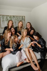 A bride and her bridal party in getting ready robes. Everyone is looking at smiling at the brides ring.