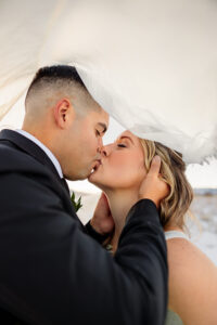 Couple portrait on their elopement day. Under a vail, holding each other, and kissing. Captured by Michelle Betz Photography