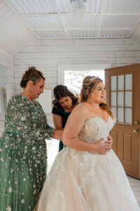 bride putting on her wedding dress with the help of mother and friend.