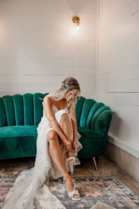 A bride putting on her wedding day shoes. She is sitting on a cute green couch. Captured by Colorado Wedding Photographer, Michelle Betz