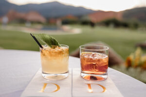 Detail wedding photo of "his and her" drinks. Surrounded by summer time beauty of green grass and Garden of the Gods