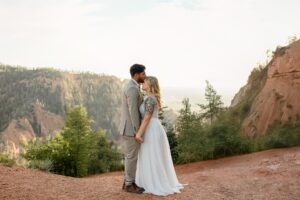 Bride and groom portrait with the couple holding hands and the groom kissing his bride on the forhead. Surrounded by Coloado Springs mountains.