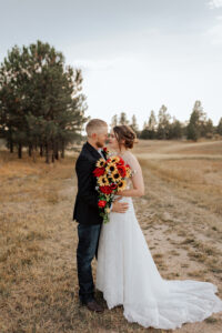 Bride and groom looking at each other portrait. Surrounded by Colorado trees and open field.