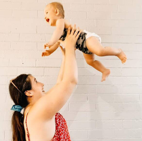 A women throws a baby into the air playfully, they are both laughing.