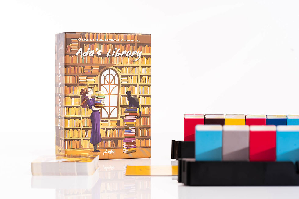 A woman holding onto a stack of books with a black cat sitting atop a pile of books as a library looms in the background of the box. In the right foreground, the Game Rack has several coloured cards on it.