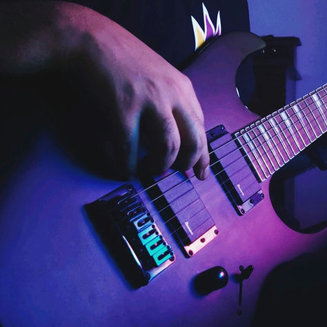 a close-up of a person playing an Ibanez electric guitar bathed in purple light
