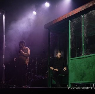 Mike Skinner seated on a Link Seating stadium seat during a live performance on The Streets tour bus shelter set.