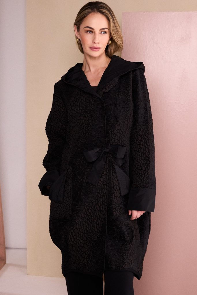 Thumbnail: Model wearing NAYA Autumn Winter 2026 Choco longline jacquard coat with hood and statement tie fastening