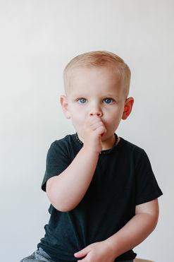 Meliza Orellana Photography_Daycare_and_schools_photography_Page_Vancouver Family Photographer_Portrait photo of a baby boy around one year old wearing a short-sleeve black shirt, looking at the camera with his right hand covering his mouth