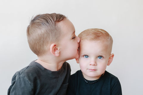 Meliza Orellana Photography_Daycare_and_schools_photography_Page_Vancouver Family Photographer_Two boys wearing round-neck dark t-shirts; the boy on the left is giving a kiss on the forehead of the boy on the right