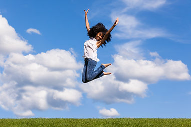 Outdoor portrait of a smiling teenage black girl jumping over a blue sky - African people.