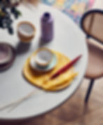 Modern table with stacked bowls, a purple vase, yellow and red dried grasses, and a colorful rug. Cozy, artistic dining setting. Professionally styled by Lucy Gough, London